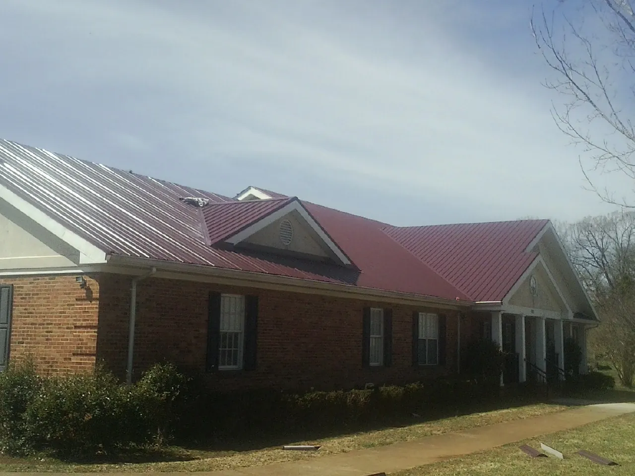 Red metal roof with gabled entries on a long brick building, from a Hail Damage Roof Repair job in Churubusco