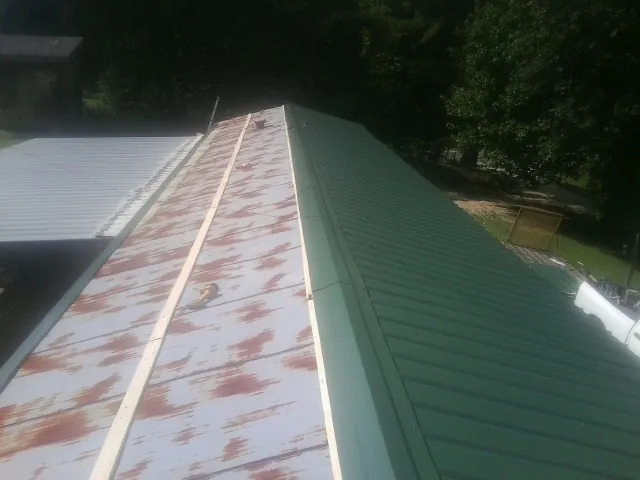 Old rusted panels beside newly installed green metal roofing — Wind Damage Roof Repair by Roofing Brothers in Churubusco
