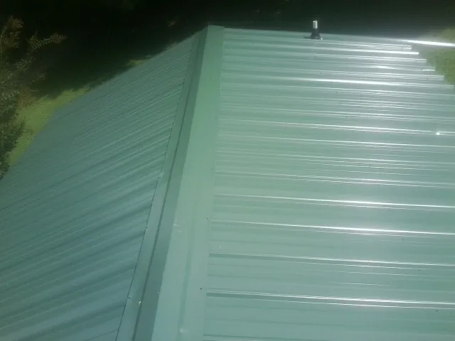 New green metal panels meeting at the ridge of a roof — Flat Roof Repair work by our crew in Churubusco