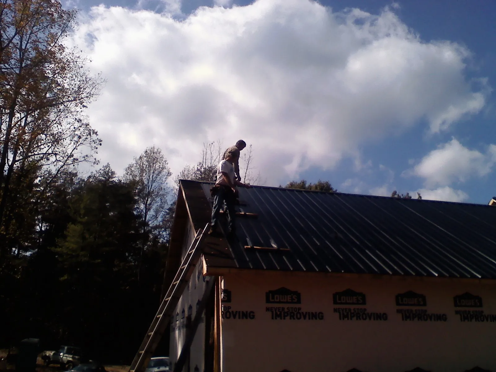 Roofer fastening dark metal panels high against a cloudy sky, from a Roof Inspection job in Churubusco