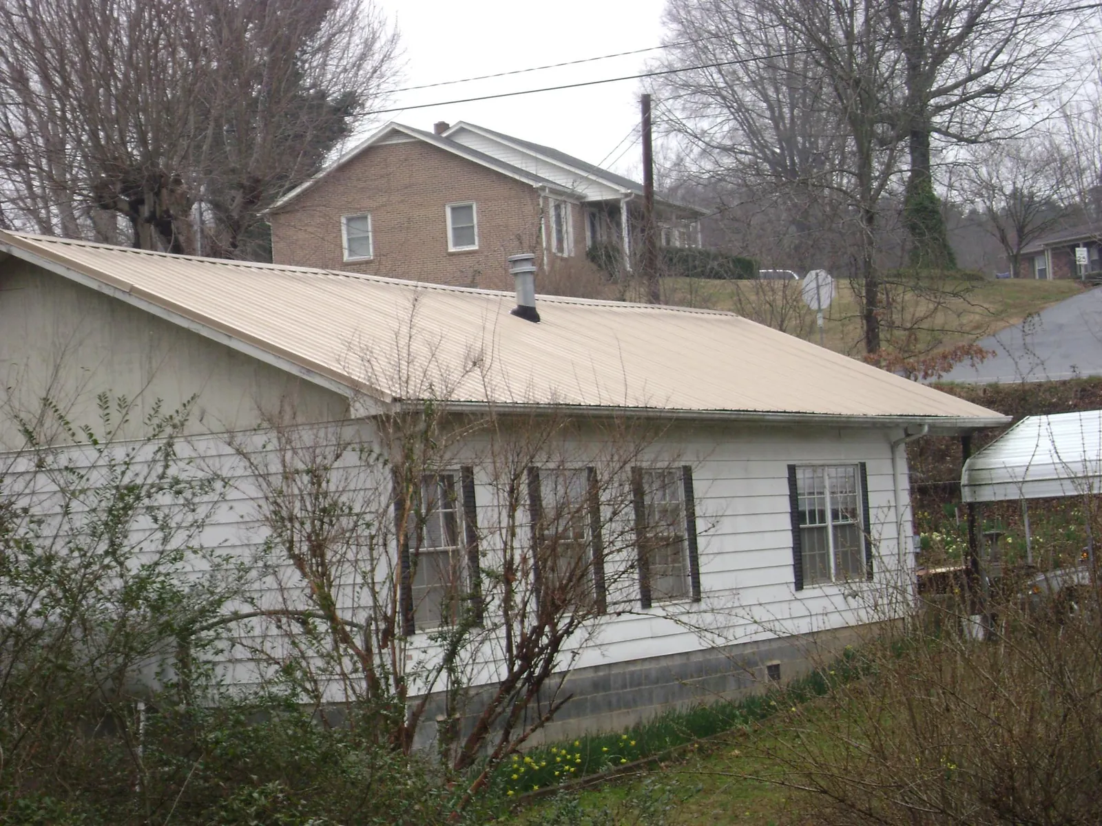 Tan metal roof on a white sided house set into a hillside — Commercial Roofing by Roofing Brothers in Churubusco