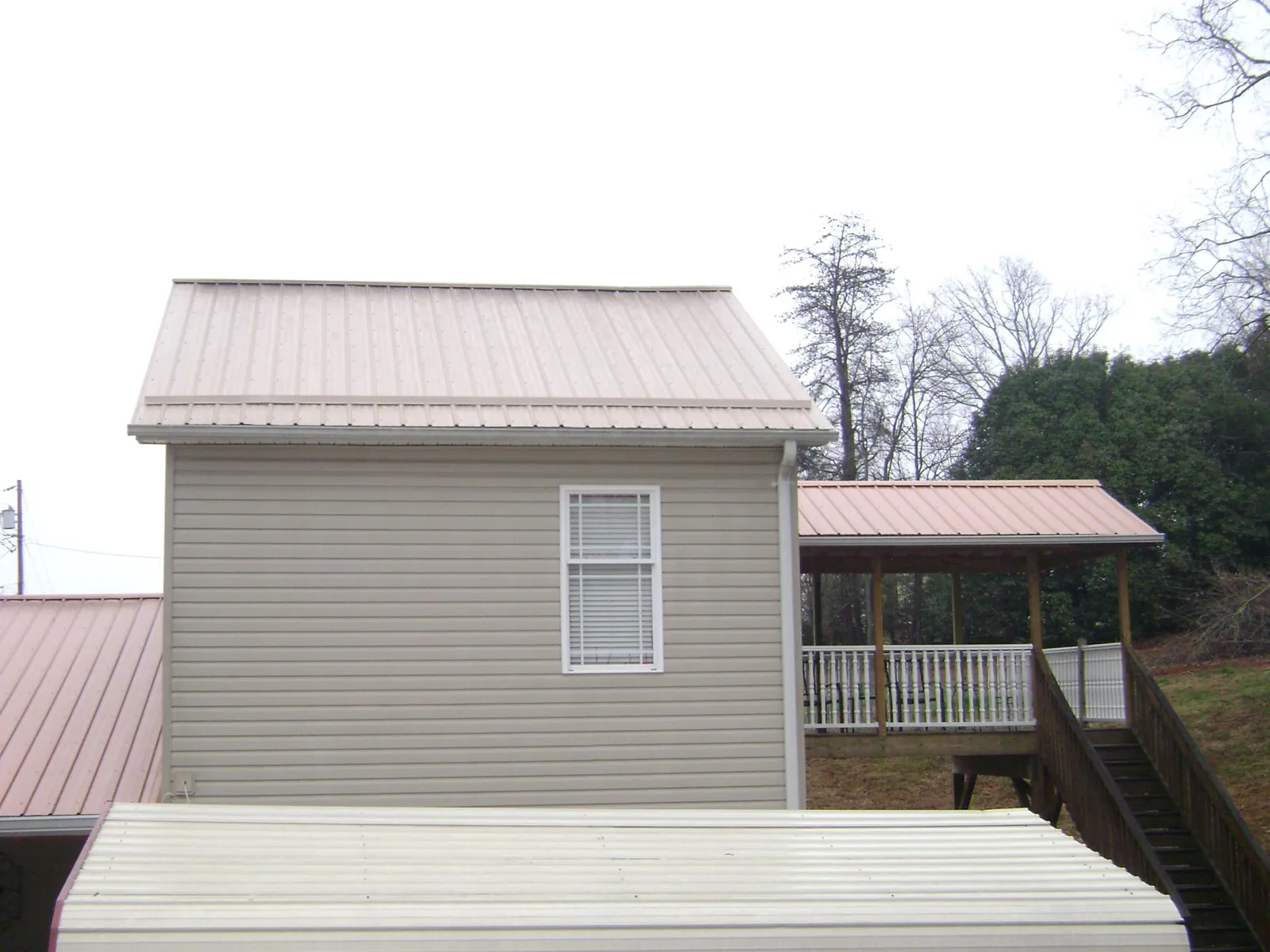 Tan metal roofs on a two story addition and attached porch, from a Roof Replacement job in Churubusco